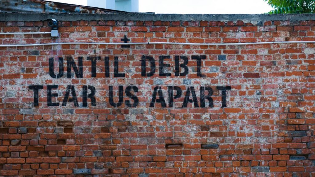 A "until debt tear us apart" graffiti written on a brick wall