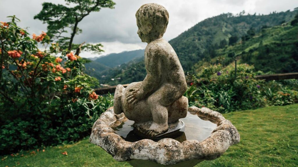 An old stone statue of a boy in a lush garden