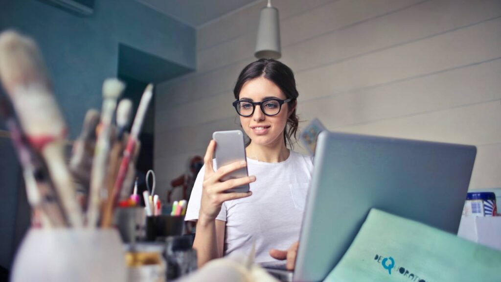 A young woman with glasses using a smartphone in her art studio 