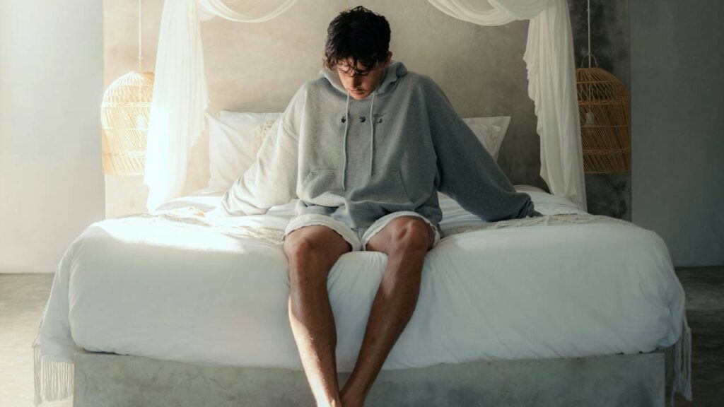 A photo of a young man sitting on a comfortable hotel bed